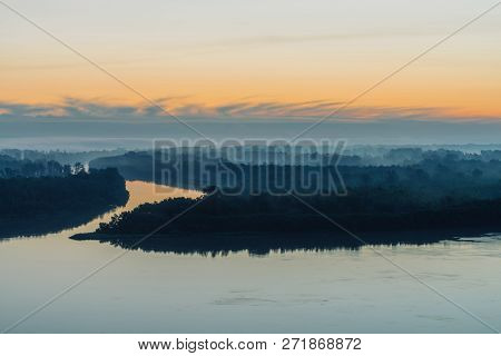 Early Blue Sky Reflected In River Water. Riverbank With Forest Under Predawn Sky. Yellow Stripe In P