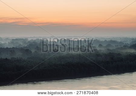 Mystical View On Riverbank  Of Large Island With Forest Under Haze At Early Morning. Eerie Mist Amon