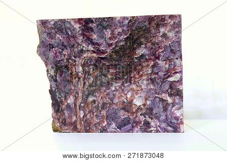 A Sample Of Charoite In The Form Of A Polished Plate On A White Table.