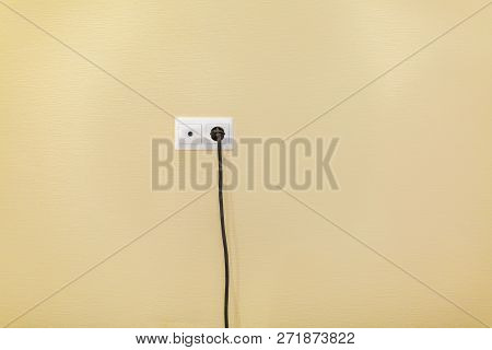 An Electrical Socket And Tv Outlet On Wall With Connected Electrical Black Cable Of Electrical Devic