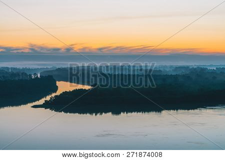 Broad River Flows Along Coast With Forest Under Thick Fog. Early Blue Sky Reflected In Water. Yellow
