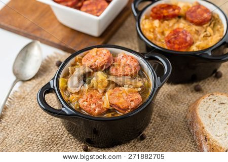 Slovak Christmas National Cabbage Soup In Two Small Black Pots With Sausage On The Tablecloth Backgr