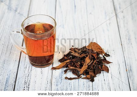 Cup Of Hot Black Tea And Dried Tea Leaves On Wooden Table