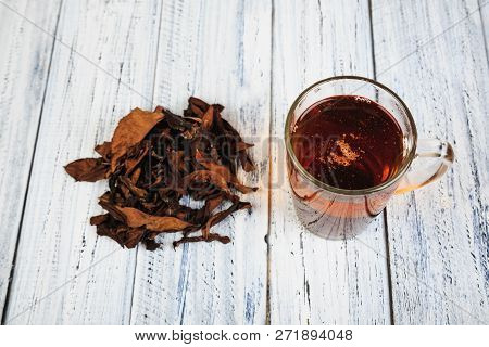 Cup Of Hot Black Tea And Dried Tea Leaves On Wooden Table Top View