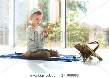 Little Muslim Boy With Misbaha And Koran Praying On Rug Indoors