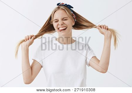 Studio Shot Of Overjoying Good-looking Happy Teenage Girl In Headband And White T-shirt Pulling Hair