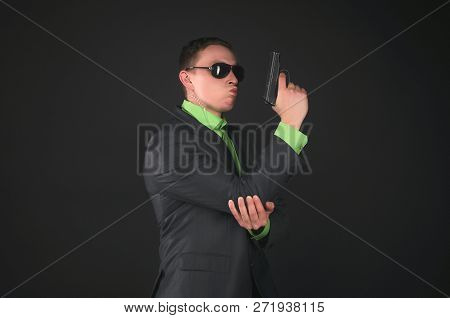 Arrogant Security Agent Is Posing With A Gun In Hand Like A Super Spy Isolated On Black Background.