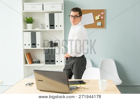 Business, Office, People Concept - Handsome Man In Glasses Stands In The Office Near A Computer And 