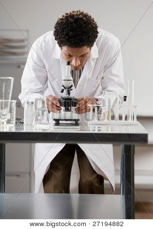 Cientista médico vestindo jaleco olhando a amostra através de microscópio no laboratório
