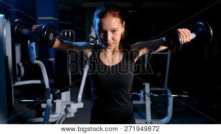 The Girl Is Engaged In The Gym. Exercise On The Deltoid Muscles With A Dumbbell.