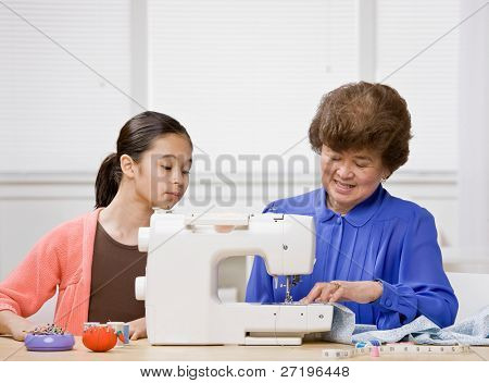 Curious granddaughter watching creative grandmother use sewing machine to make clothing