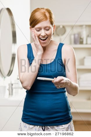Excited, happy woman in bathroom viewing positive pregnancy test