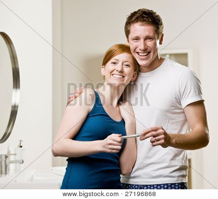 Excited, happy couple in bathroom viewing positive pregnancy test