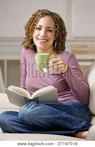 Relaxed women enjoying reading a book in livingroom while drinking tea