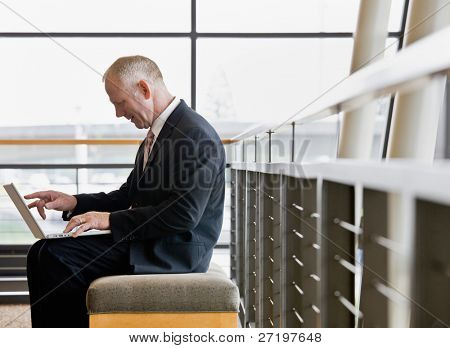 Olgun işadamı, ofis lobisinde bir dizüstü bilgisayarda çalışan yan görünüm