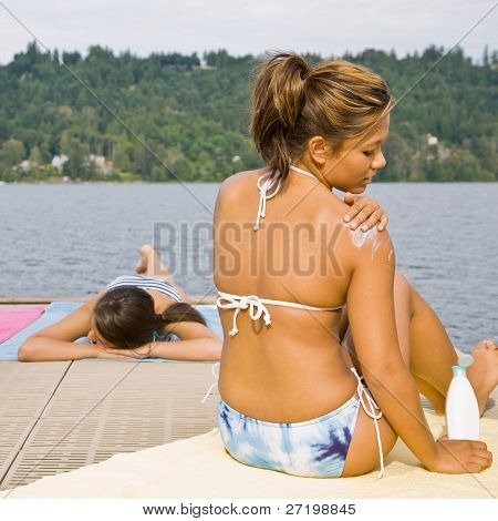 Femme assise sur la jetée, application de lotion écran solaire