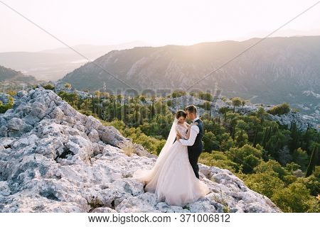 A Wedding Couple Stands On Top Of A Mountain With Panoramic Views Of The Bay Of Kotor, At Sunset. Th