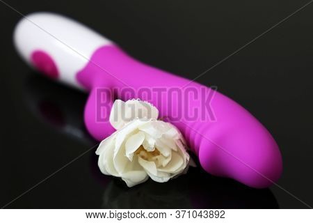 Dildo And White Rose On A Dark Glass Background, Romantic Gift For Sex. Wet Flower And Purple Silico