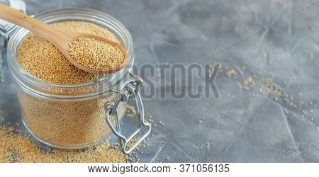 Jar Of Raw Amaranth Seeds With A Spoon On A Grey Table Close Up With Copy Space