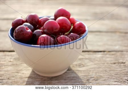 Ripe Black Cherries With Water Drops In A White Ceramic Bowl With A Blue Border On A Wooden Table Ba
