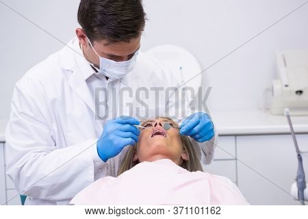 Dentist holding equipment while cleaning woman teeth at medical clinic