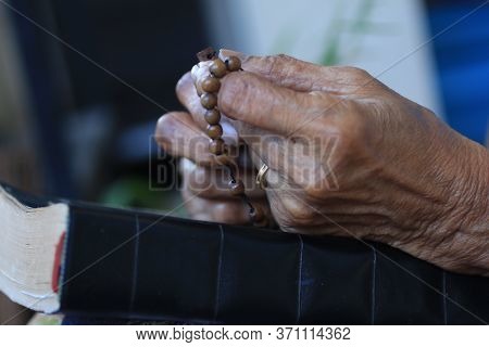 Hands Of Asia Senior Woman Holding Rosary On Bible Book. A Spiritual Grandmother Praying Rosary Clos