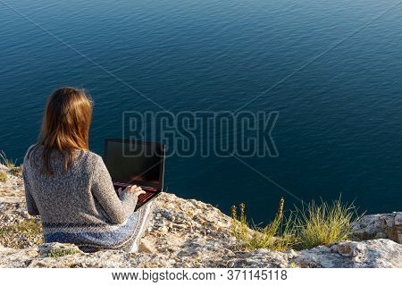 A Girl Is Working On A Laptop At The Top Of A Mountain. Remote Work And Training In Nature. Sea View