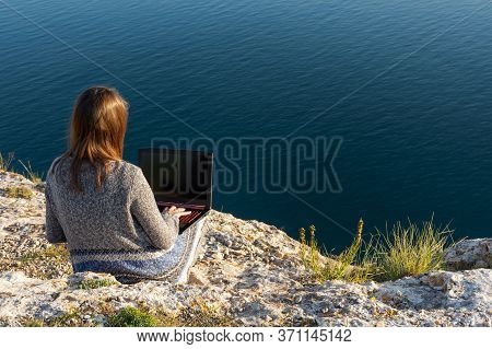A Girl Is Working On A Laptop At The Top Of A Mountain. Remote Work And Training In Nature. Sea View