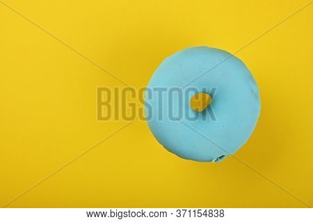 Close Up One Blue Glazed Ring Donut Over Yellow Background, Elevated Top View, Directly Above