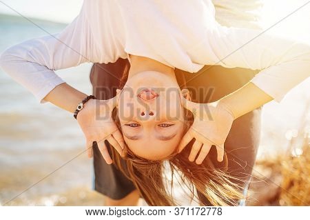 Little School Age Girl Hanging Upside Down, Making Faces. On A Lake Shoreside.