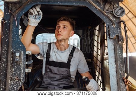 A Man In Overalls Driving A Tractor. Worker Sitting On His Tractor