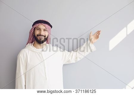Attractive Smiling Arab Man Points His Hand To A Gray Background