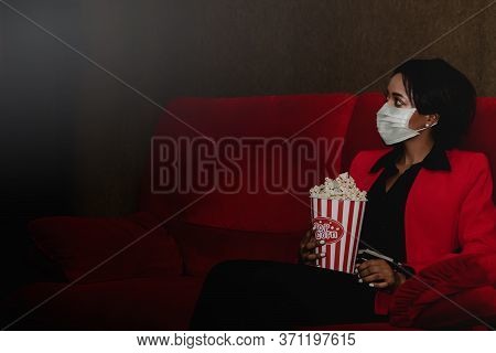 African-american Woman Wears A Germ Protection Mask And Sits With Popcorn To Eat On The Luxurious Re