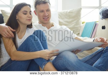 Young couple moving in to new home together, sitting on The floor and diskuss plan of desing.