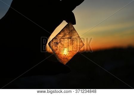 A Close Up Image Of Transparent Champagne Calcite Held Against A Glowing Orange Sunset.
