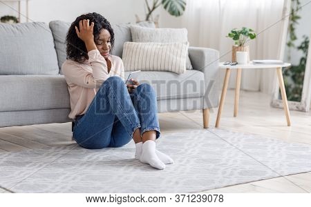Heartbroken Girl. Upset Crying Black Woman Sitting With Smartphone On Floor At Home, Feeling Lonely 