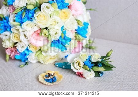 Gold Wedding Rings Lie Next To The Boutonniere And Wedding Bouquet. Wedding Bouquet With White Eusto