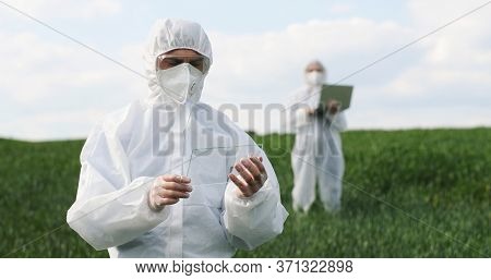 Caucasian Man Scientist In Protective Costume Standing In Field, Tapping On Glass As On Screen Of Fu