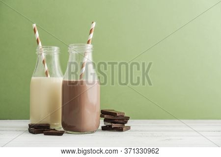 Two Bottles Chocolate And Vanila Milk With Drinking Straws On Green Background