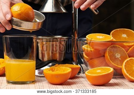 Squeezing an orange with a manual press, close view, making a glass of fresh. Fresh oranges on a wooden table, whole, squeezed and sliced.