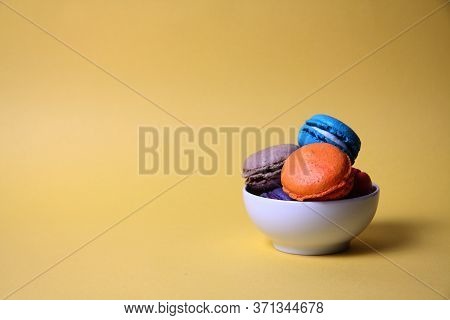 Macaroons Of Differrent Colours In A Bowl Isolated On Yellow Background. Image Contains Copy Space