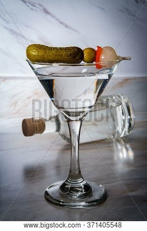 Dry Gin Martini Served Neat With Pickle Cocktail Stirrer And Bottle In Background