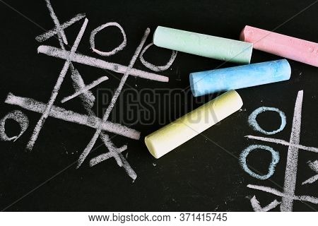 A Close Up Image Of A Tic-tac-toe Game Done In Brightly Colored Chalk On A Black Background.