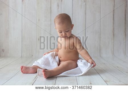 One Yeat Old Baby Girl Is Sitting On Wooden Backgroun In White Towel. After Bath Time.
