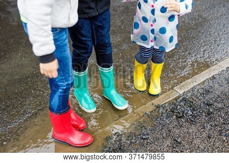 Close-up Of Three Children, Toddler Girl And Two Kids Boys Wearing Red, Yellow And Green Rain Boots 