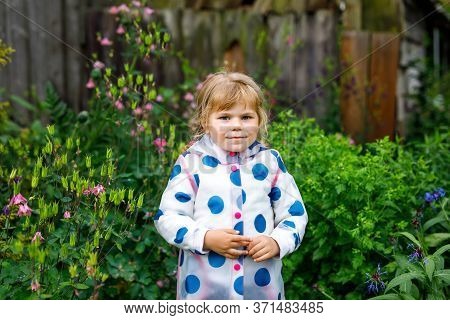 Outdoor Portrait Of Happy Smiling Little Toddler Girl Wearing Rain Jacket On Rainy Cloudy Day. Cute 