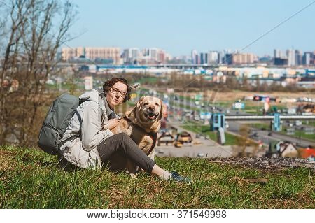 A girl sits hugging a Labrador Retriever on a mountain against the background of the city. Vacation 