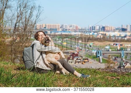 A Girl Sits Hugging A Labrador Retriever On A Mountain Against The Background Of The City. Vacation 