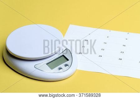White Home Scales Next To The Calendar. Weighing And Date Marking