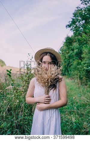 Happy Young Woman In A White Dress In A Straw Hat. Smiling Girl With A Bouquet Of Dried Flowers. Gir